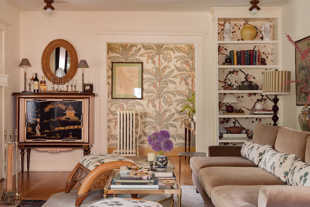 Living room with brown velvet sectional, botanical wallpaper, and collected art