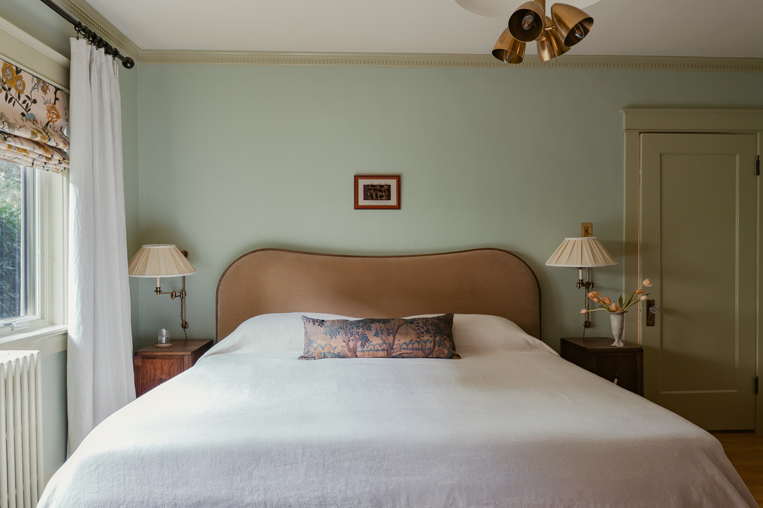 Sage green bedroom with curved upholstered headboard and brass sconces