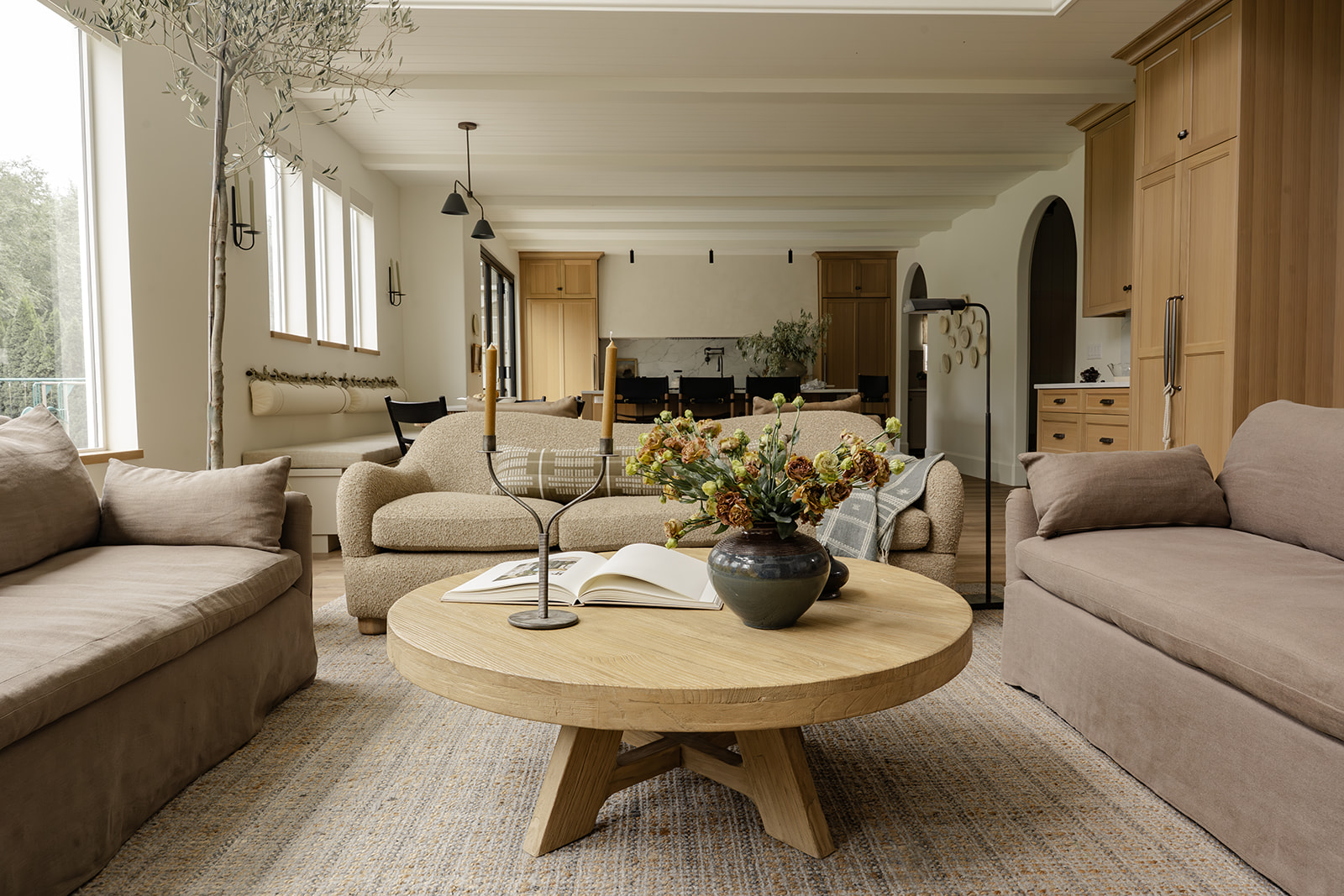 Living room with boucle sofas, round oak coffee table, and olive tree