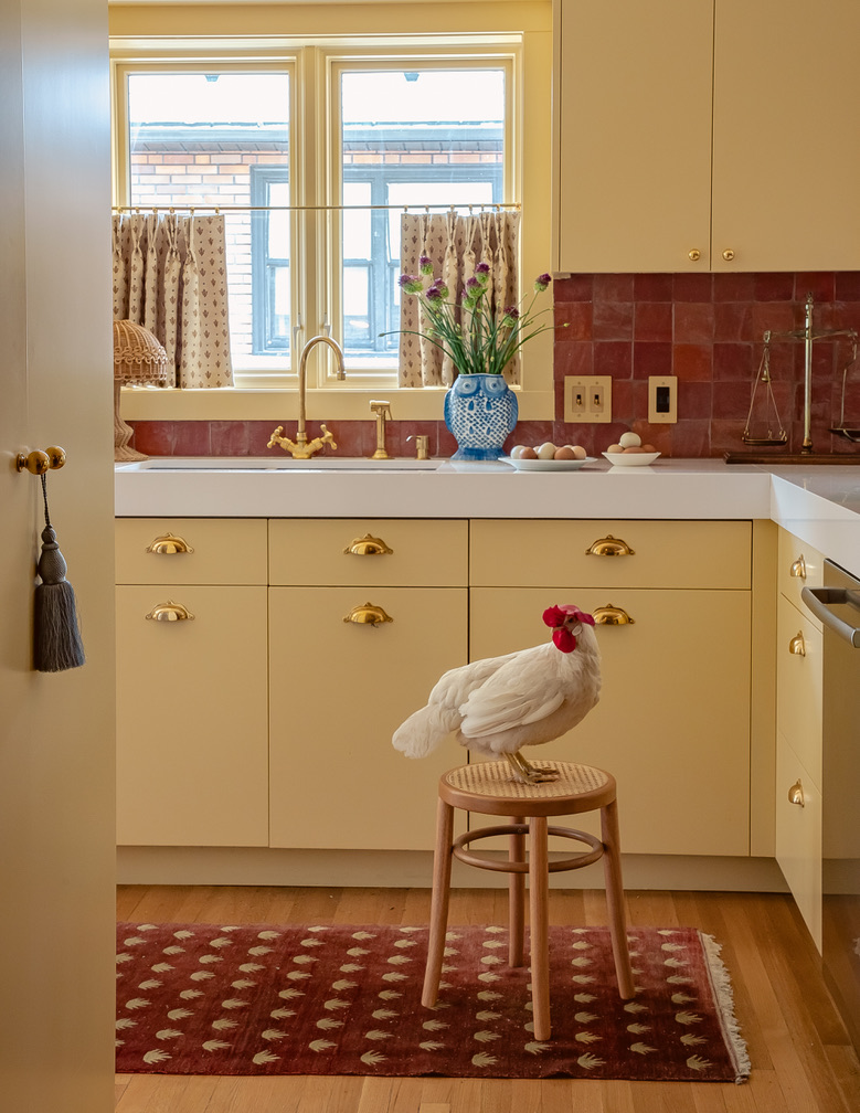 Butter-yellow kitchen with brass hardware and terracotta tile backsplash