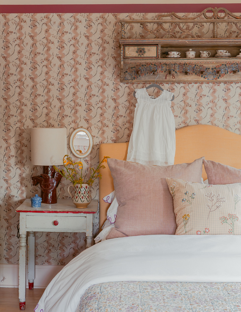 Guest bedroom with floral wallpaper, antique shelf, and layered pink bedding